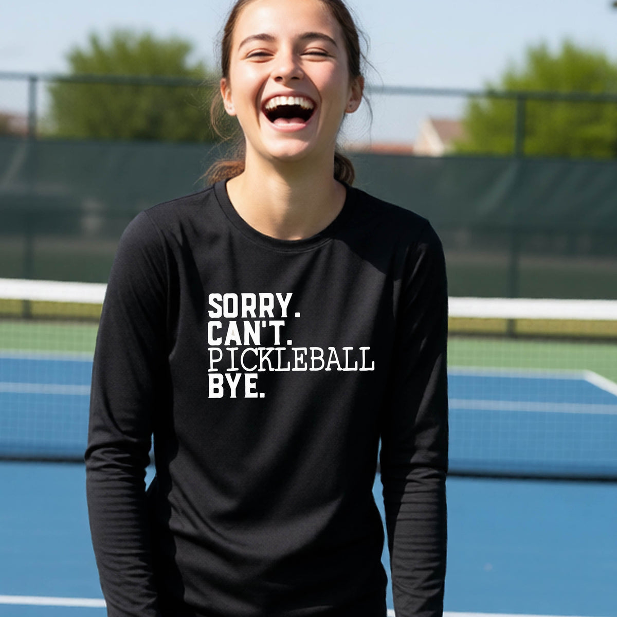 A young person on a pickleball court wearing a black short-sleeve t-shirt with a white graphic of the words  “SORRY. CAN’T. PICKLEBALL BYE” each on a separate line, on the front of the shirt.