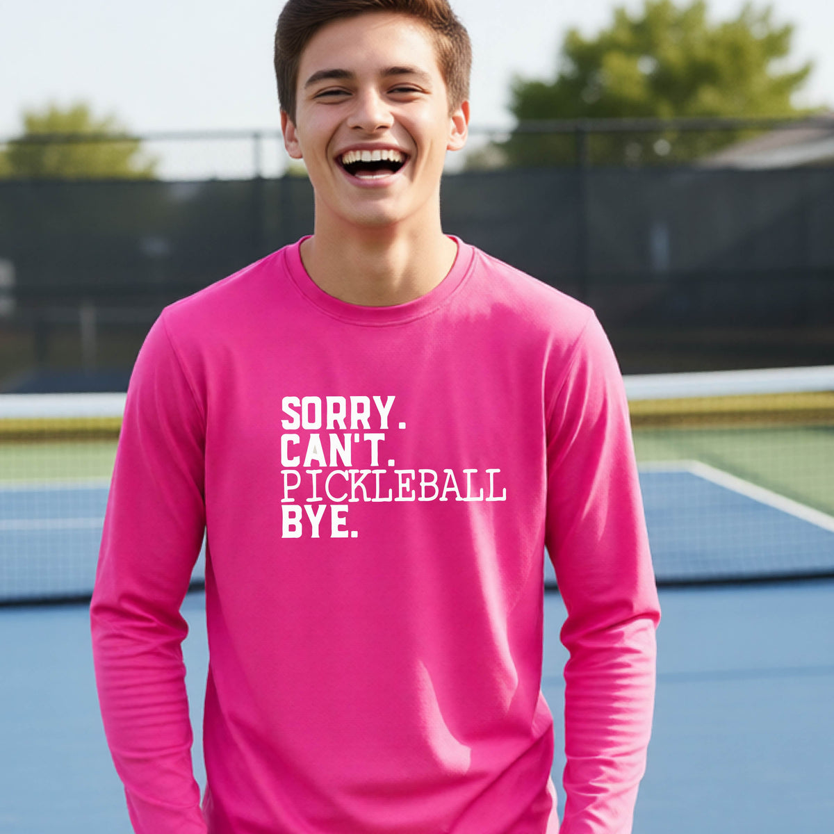 A young person on a pickleball court wearing a pink short-sleeve t-shirt with a white graphic of the words  “SORRY. CAN’T. PICKLEBALL BYE” each on a separate line, on the front of the shirt.