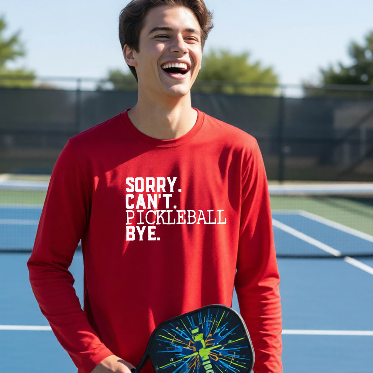 A young person on a pickleball court wearing a red short-sleeve t-shirt with a white graphic of the words  “SORRY. CAN’T. PICKLEBALL BYE” each on a separate line, on the front of the shirt.