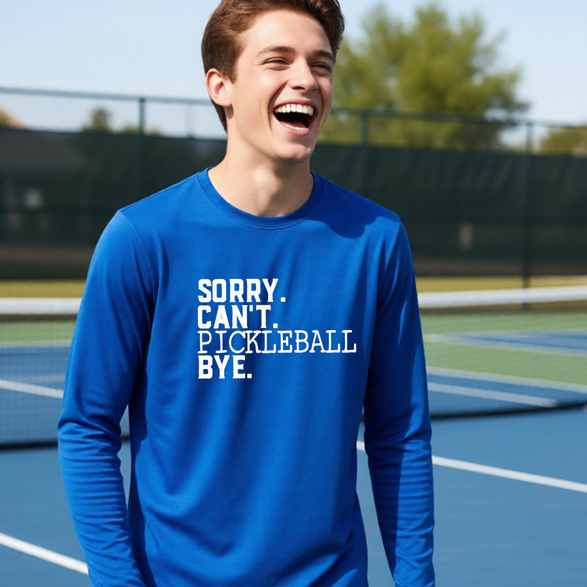 A young person on a pickleball court wearing a royal blue short-sleeve t-shirt with a white graphic of the words  “SORRY. CAN’T. PICKLEBALL BYE” each on a separate line, on the front of the shirt.