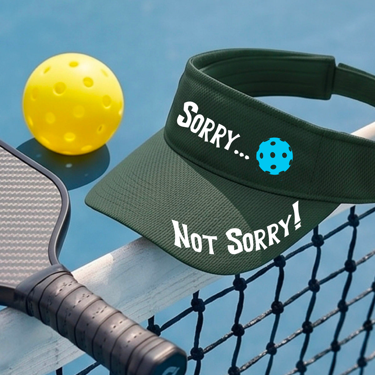 A close-up of a green athletic visor with motif.design on the front and brim..  The front features the playful word “SORRY…” in bold white lettering, accented a colorful pickleball, and the brim design features “NOT SORRY!” in bold white lettering curved around the brim edge.