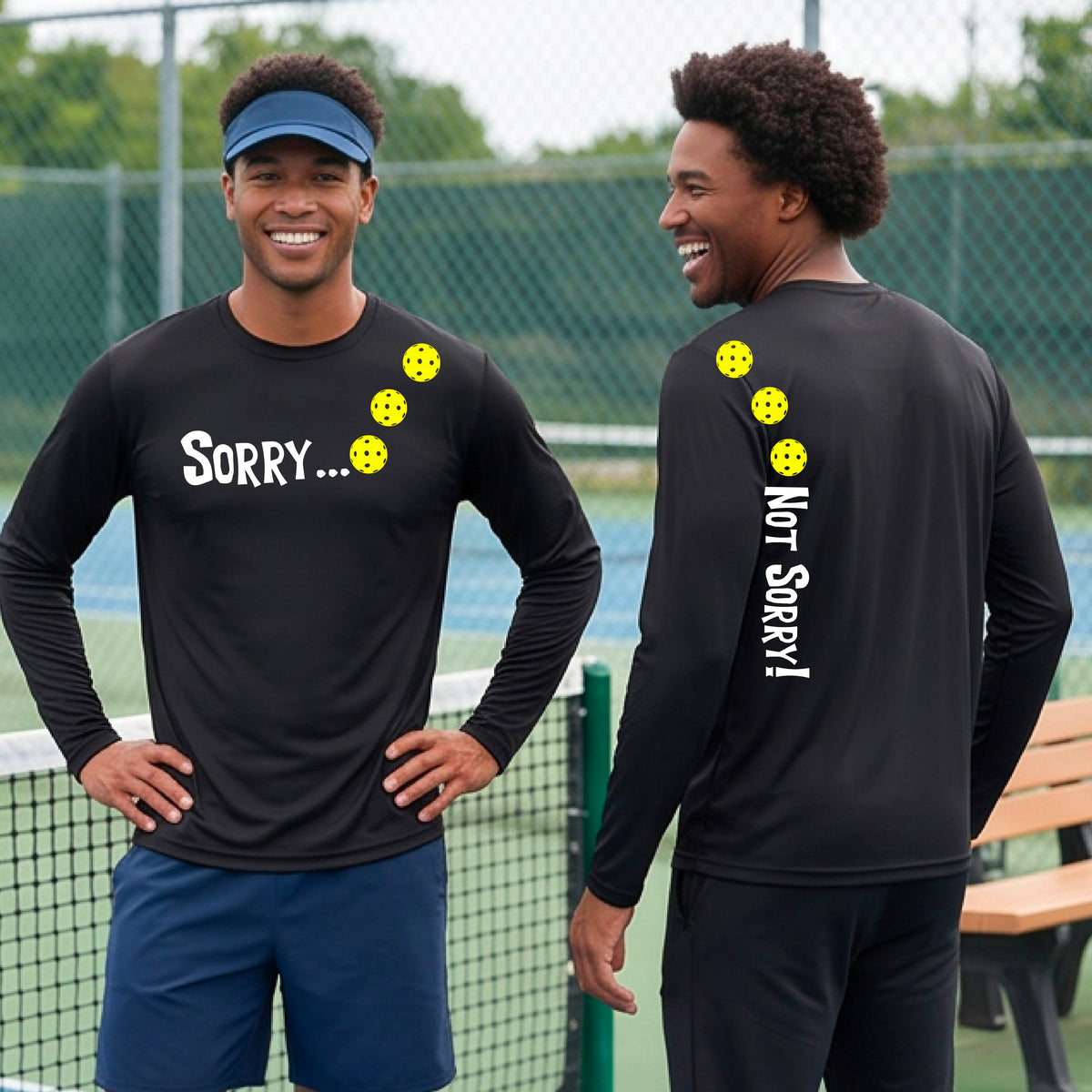 Two men on a pickleball court wearing black long-sleeve t-shirts with a front/back graphic design.  The front features the playful word “SORRY…” in bold white lettering, accented with three colorful pickleballs arranged diagonally across the upper chest.  The back design features “NOT SORRY!” in bold white lettering running vertically down the upper back, with three matching colorful pickleballs positioned above lettering.  