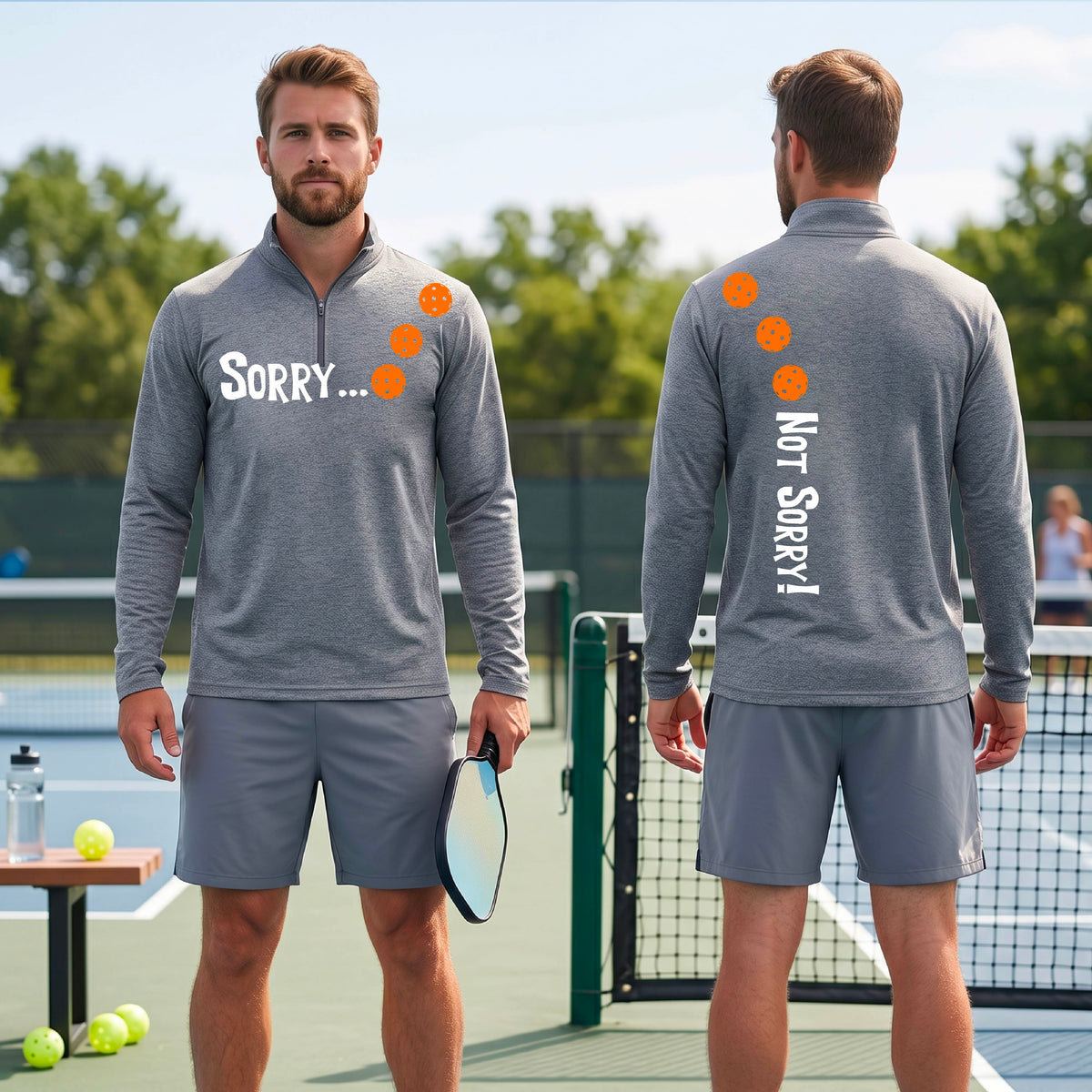 Two men on a pickleball court wearing gray quarter-zip shirts with a front/back graphic design.  The front features the playful word “SORRY…” in bold white lettering, accented with three colorful pickleballs arranged diagonally across the upper chest.  The back design features “NOT SORRY!” in bold white lettering running vertically down the upper back, with three matching colorful pickleballs positioned above lettering.  