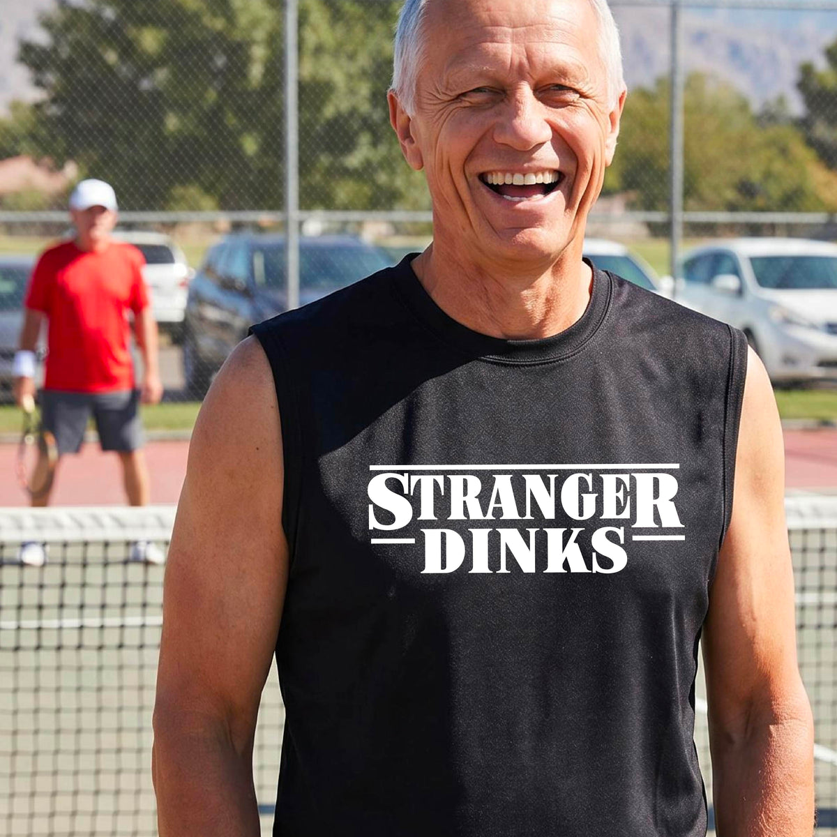 A man on a pickleball court wearing a black short-sleeve t-shirt with a white graphic of the words “STRANGER DINKS” on the front of the shirt in the style of the popular TV Series Stranger Things. 