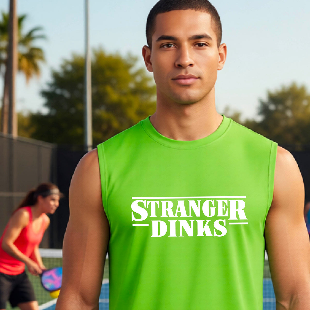 A man on a pickleball court wearing a lime green short-sleeve t-shirt with a white graphic of the words “STRANGER DINKS” on the front of the shirt in the style of the popular TV Series Stranger Things. 