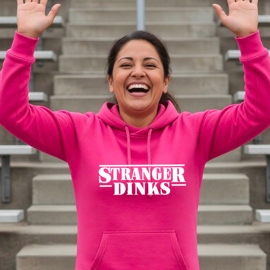 A woman wearing a black cowl-neck hoodie pullover with a white graphic of the words “STRANGER DINKS” on the front of the shirt in the style of the popular TV Series Stranger Things. 