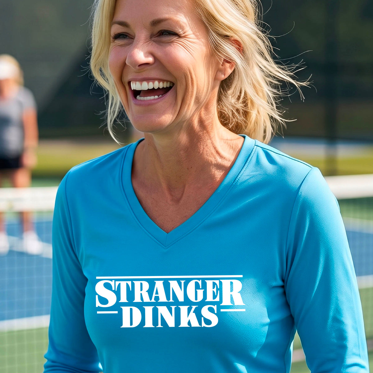 A man on a pickleball court wearing a bright blue long-sleeve t-shirt with a white graphic of the words “STRANGER DINKS” on the front of the shirt in the style of the popular TV Series Stranger Things. 