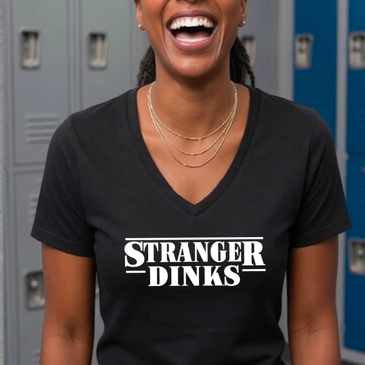 A woman wearing a black short-sleeve t-shirt with a white graphic of the words “STRANGER DINKS” on the front of the shirt in the style of the popular TV Series Stranger Things. 