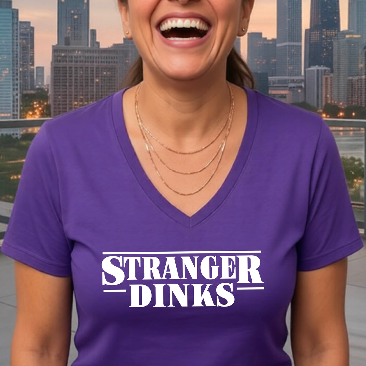A woman wearing a purple short-sleeve t-shirt with a white graphic of the words “STRANGER DINKS” on the front of the shirt in the style of the popular TV Series Stranger Things. 