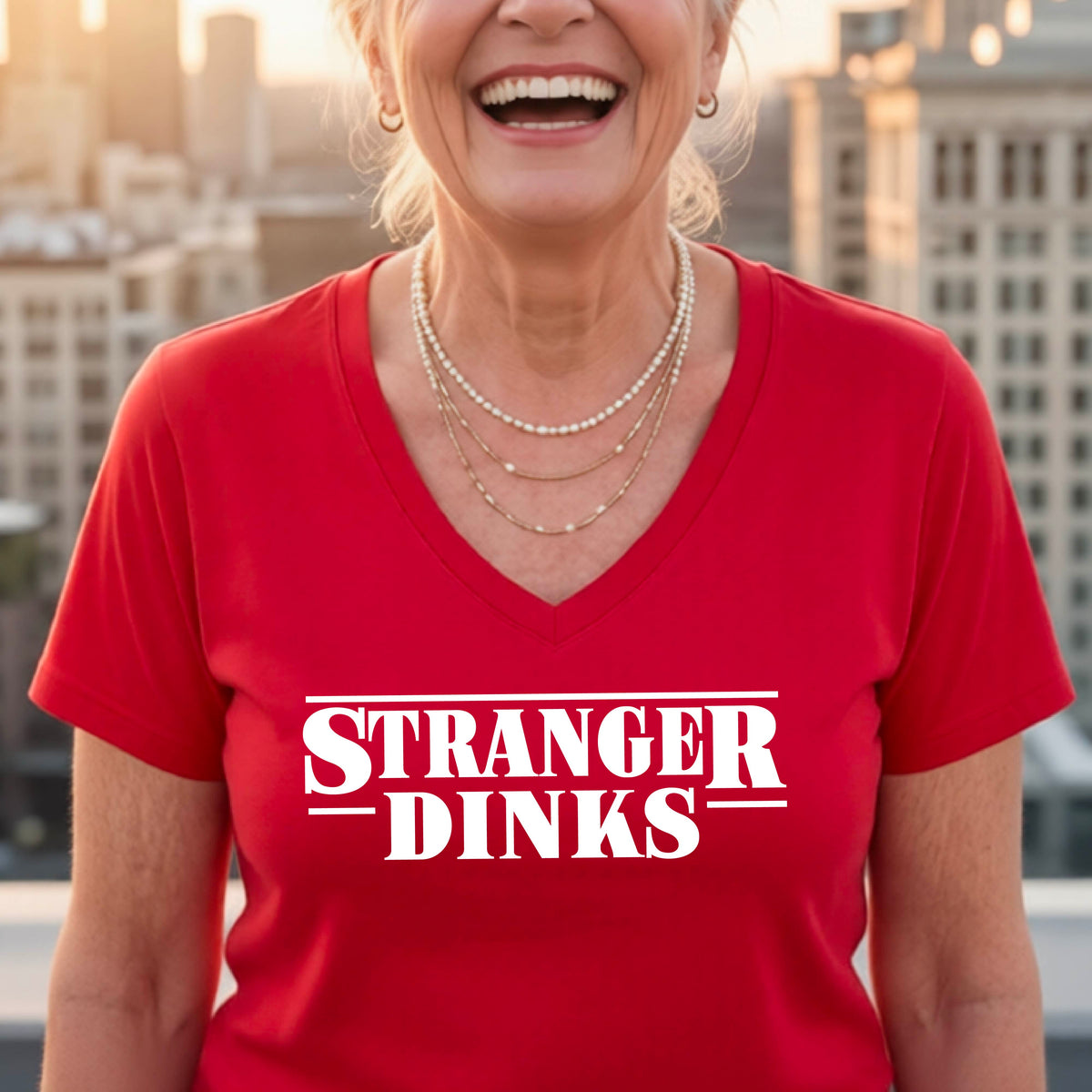 A woman wearing a red short-sleeve t-shirt with a white graphic of the words “STRANGER DINKS” on the front of the shirt in the style of the popular TV Series Stranger Things. 