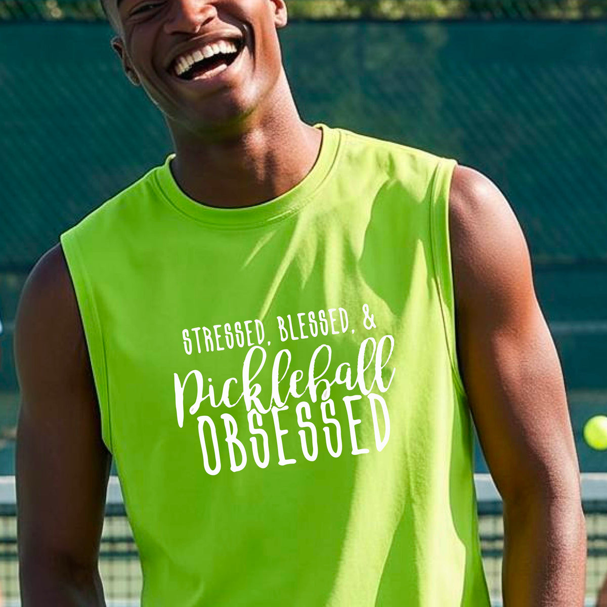 A man on a pickleball court wearing a lime green sleeveless t-shirt with a white graphic of the words “Stressed, Blessed & Pickleball Obsessed” on the front of the shirt.