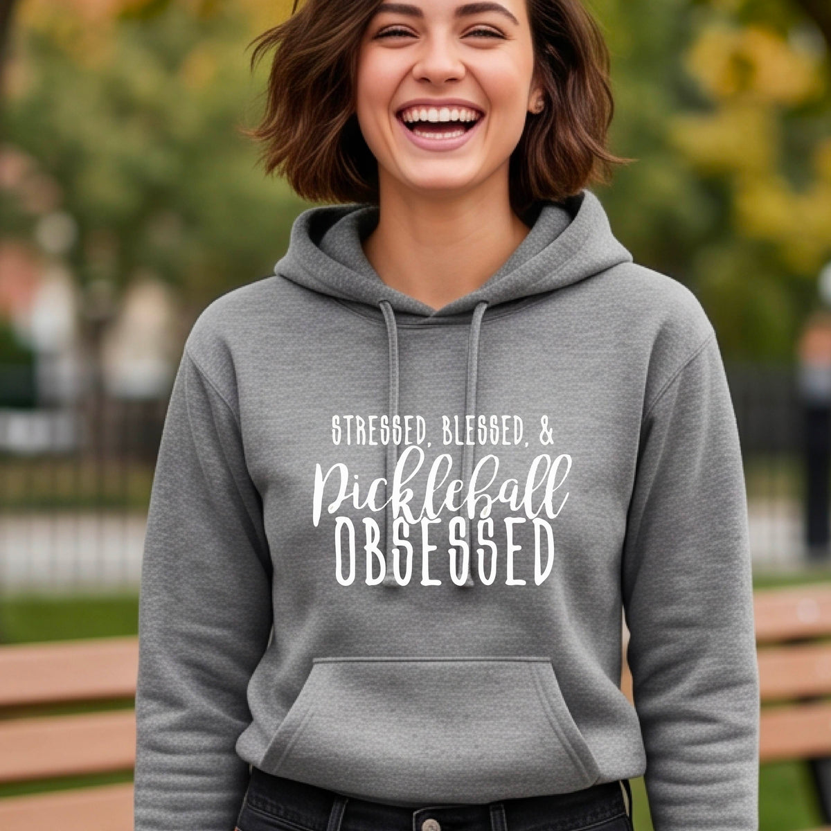 A woman wearing a gray fitted hoodie pullover with a white graphic of the words “Stressed, Blessed & Pickleball Obsessed” on the front of the hoodie.