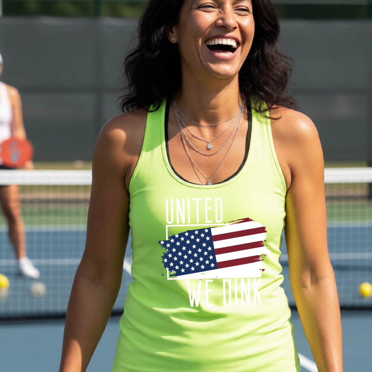 A woman on a pickleball court wearing a lime green racerback tank top with a pickleball themed red, white and blue graphic of a patriotic flag with white words “UNITED WE DINK” above and below the flag, on the front of the shirt. 