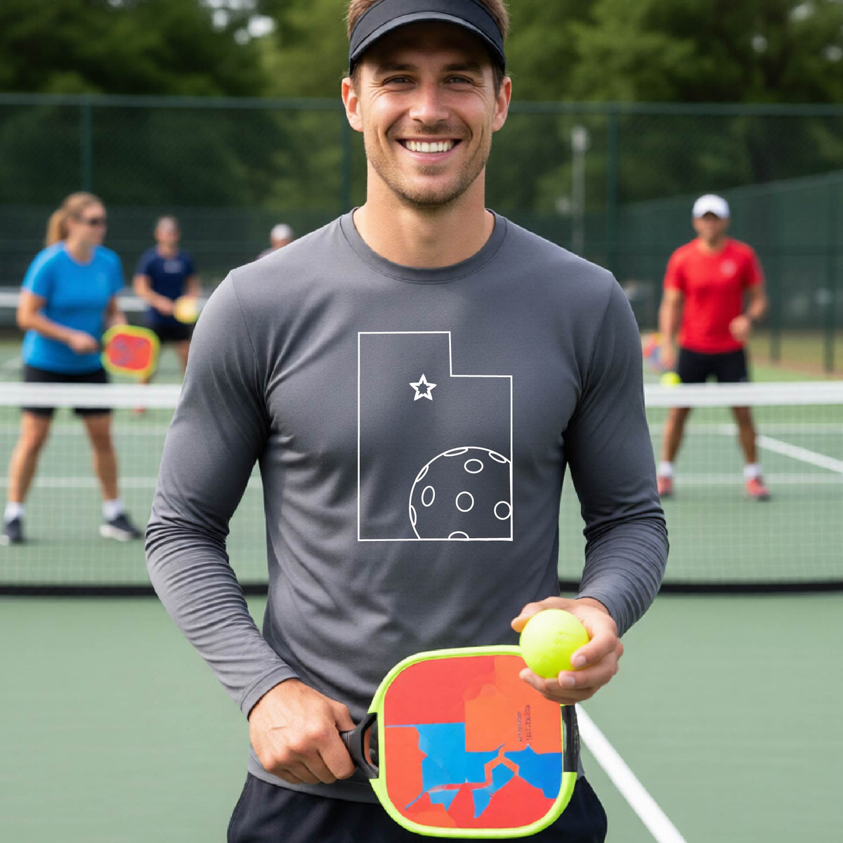 A close-up of a man wearing a dark gray short-sleeve t-shirt, with a white graphic outline of the State of Utah , including an outline of a white pickleball in the lower right corner and a star outline in the center of the graphic, on the back of the shirt.   