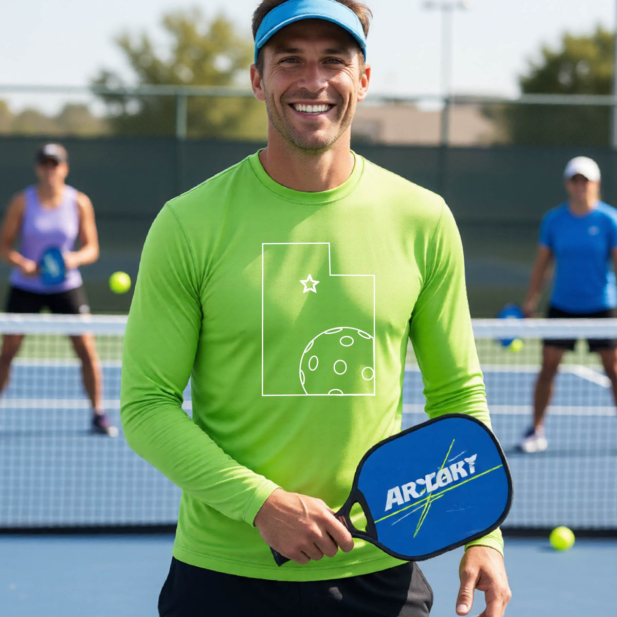 A close-up of a man wearing a lime green short-sleeve t-shirt, with a white graphic outline of the State of Utah , including an outline of a white pickleball in the lower right corner and a star outline in the center of the graphic, on the back of the shirt.   