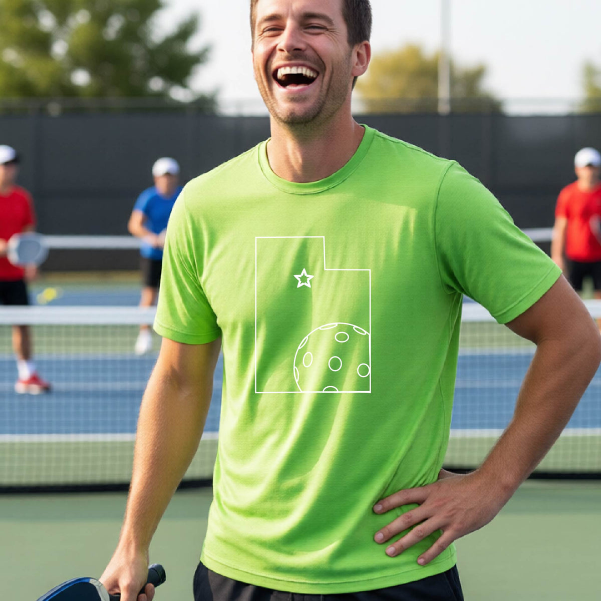A close-up of a man wearing a lime green short-sleeve t-shirt, with a white graphic outline of the State of Utah , including an outline of a white pickleball in the lower right corner and a star outline in the center of the graphic, on the back of the shirt.   