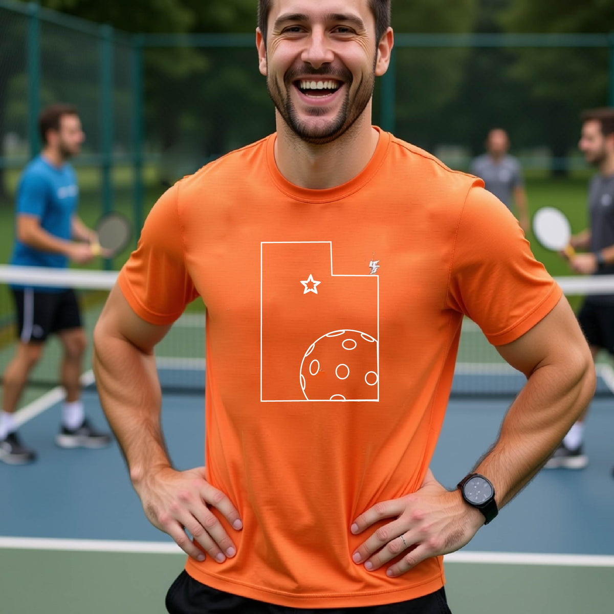 A close-up of a man wearing an orange short-sleeve t-shirt, with a white graphic outline of the State of Utah , including an outline of a white pickleball in the lower right corner and a star outline in the center of the graphic, on the back of the shirt.   