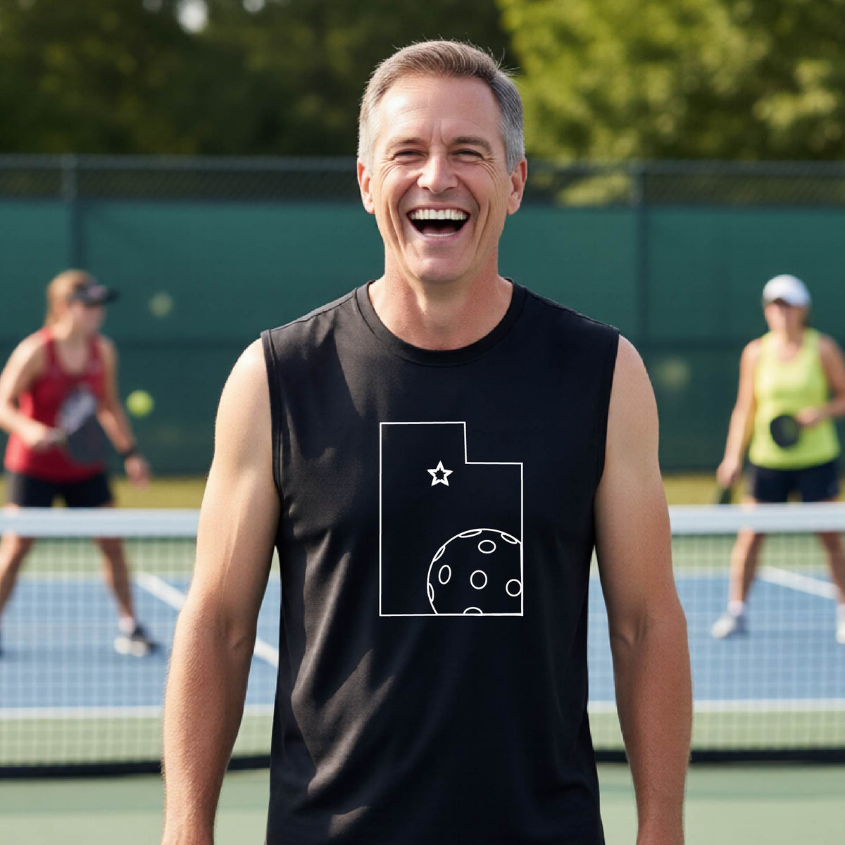 A close-up of a man wearing a black sleeveless t-shirt, with a white graphic outline of the State of Utah , including an outline of a white pickleball in the lower right corner and a star outline in the center of the graphic, on the back of the shirt.  