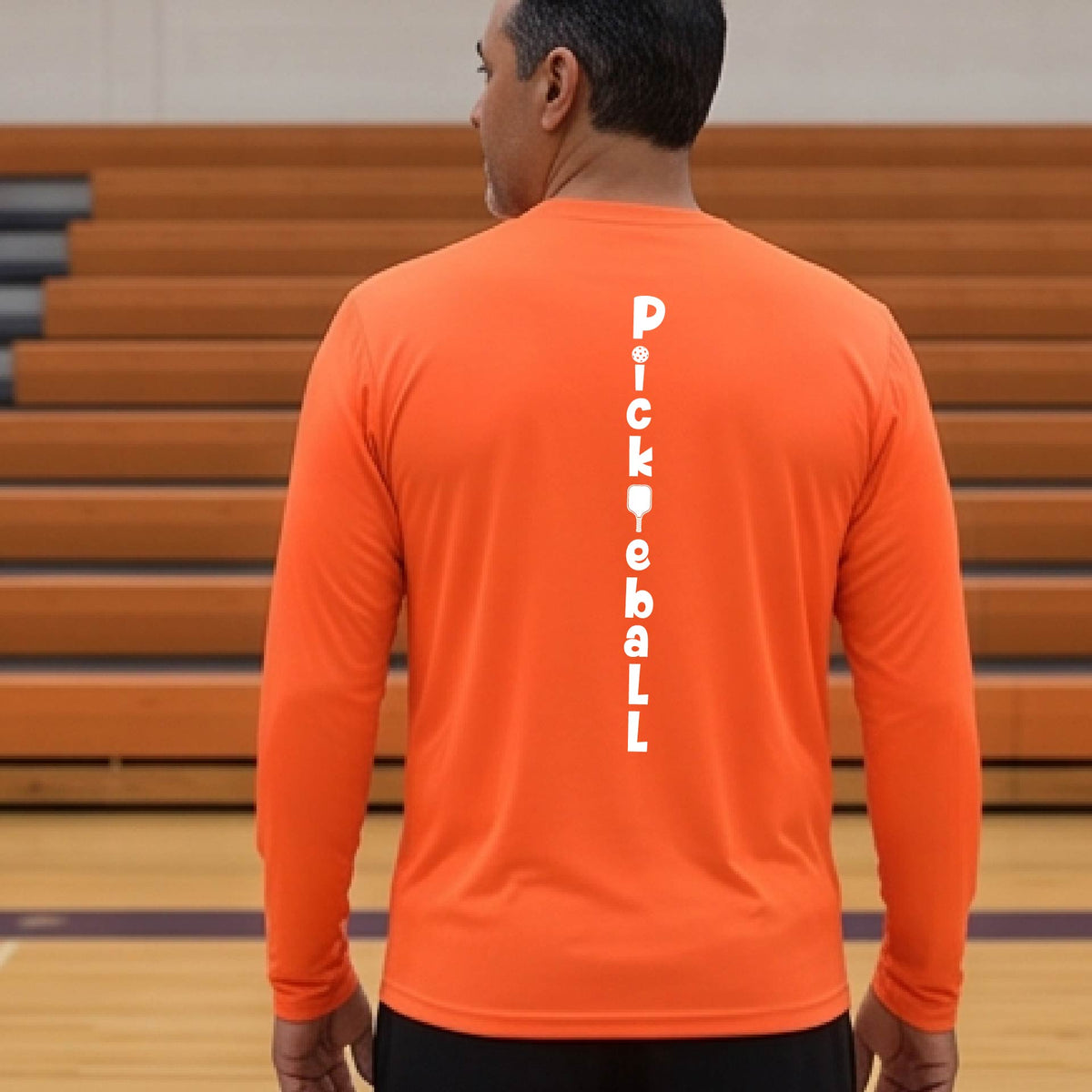 A man wearing an orange long-sleeve t-shirt with a white graphic text 'PICKLEBALL' on the back with a pickleball paddle replacing the L,.