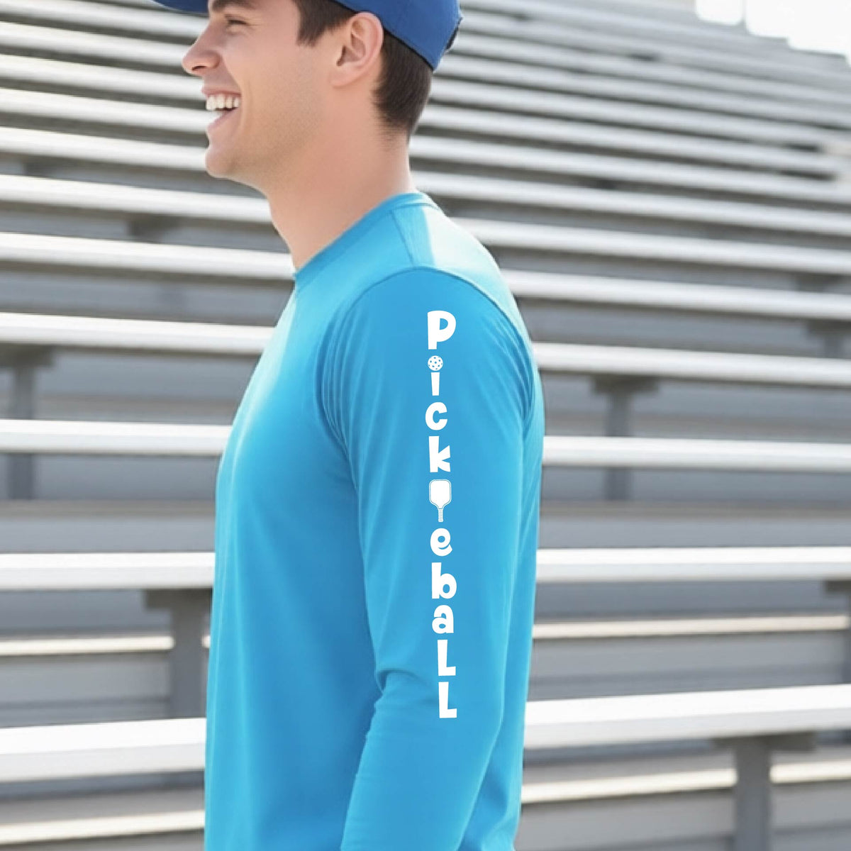A man wearing a bright blue long-sleeve t-shirt with a white graphic text 'PICKLEBALL' on the sleeve with a pickleball paddle replacing the L..