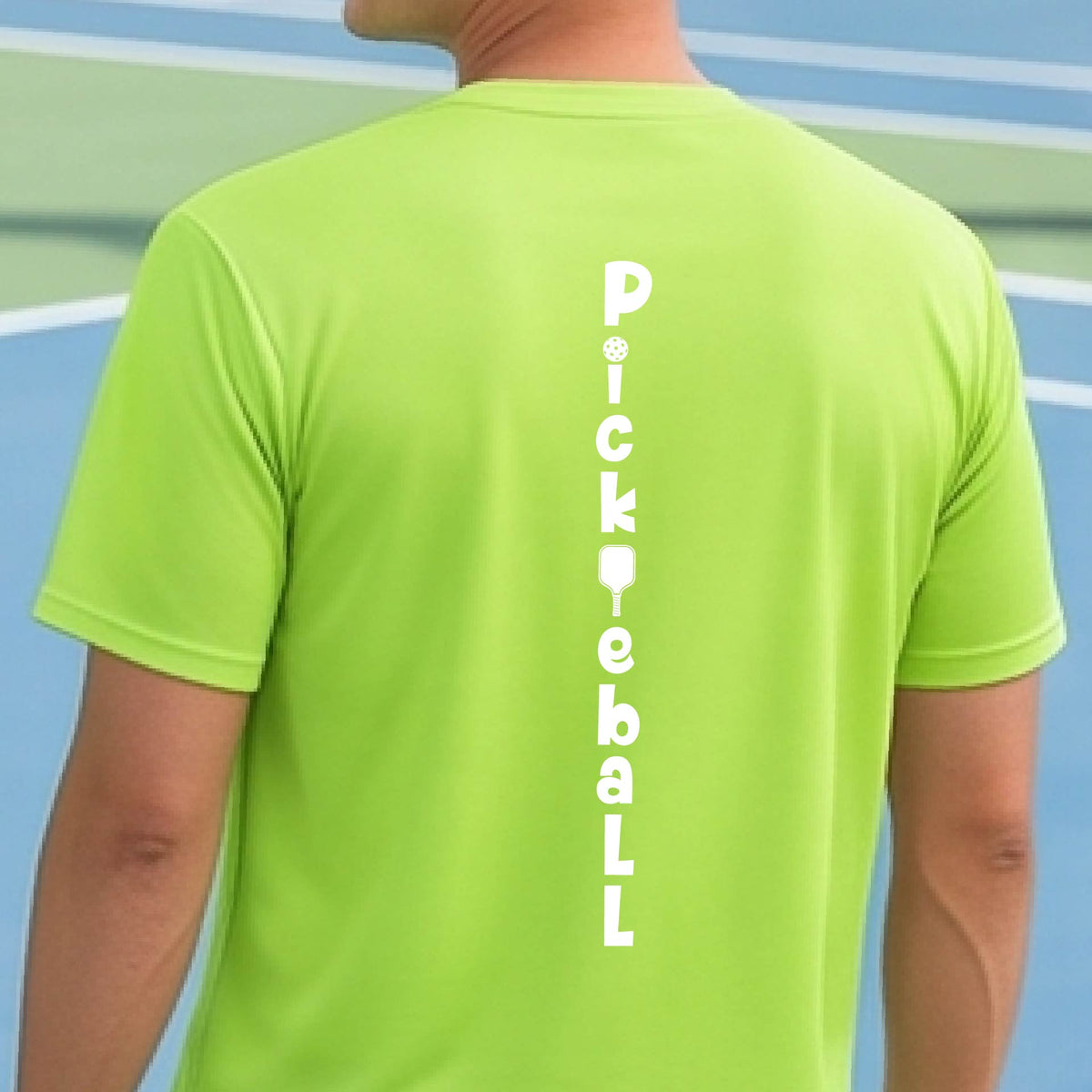 A man wearing a lime green short-sleeve t-shirt with a white graphic text 'PICKLEBALL' on the back with a pickleball paddle replacing the L, standing on a pickleball court.