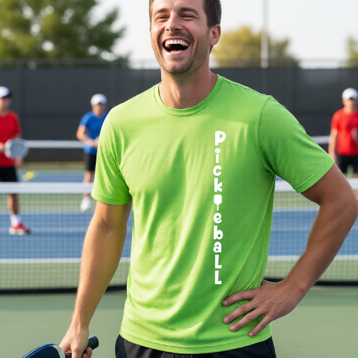 A man wearing a lime green short-sleeve t-shirt with a white graphic text 'PICKLEBALL' on the front with a pickleball paddle replacing the L, standing on a pickleball court.