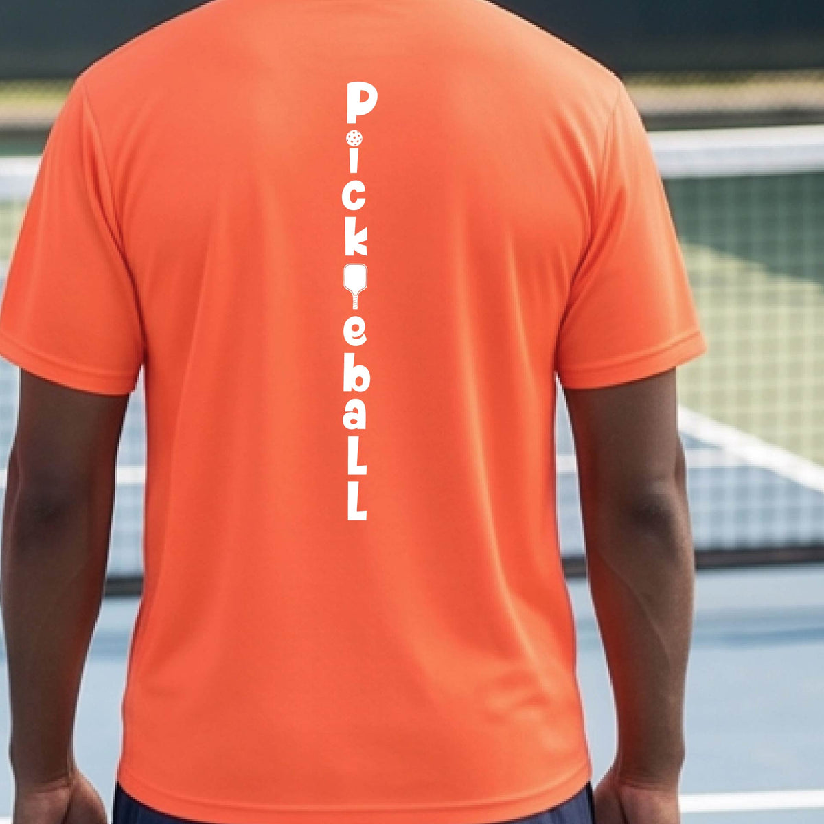 A man wearing an orange short-sleeve t-shirt with a white graphic text 'PICKLEBALL' on the back with a pickleball paddle replacing the L, standing on a pickleball court.