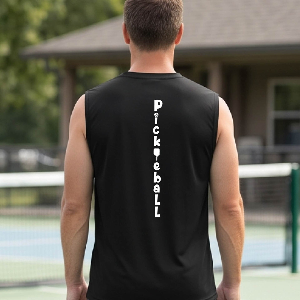 A man wearing a black sleeveless t-shirt with a white graphic text 'PICKLEBALL' on the back with a pickleball paddle replacing the L, standing on a pickleball court