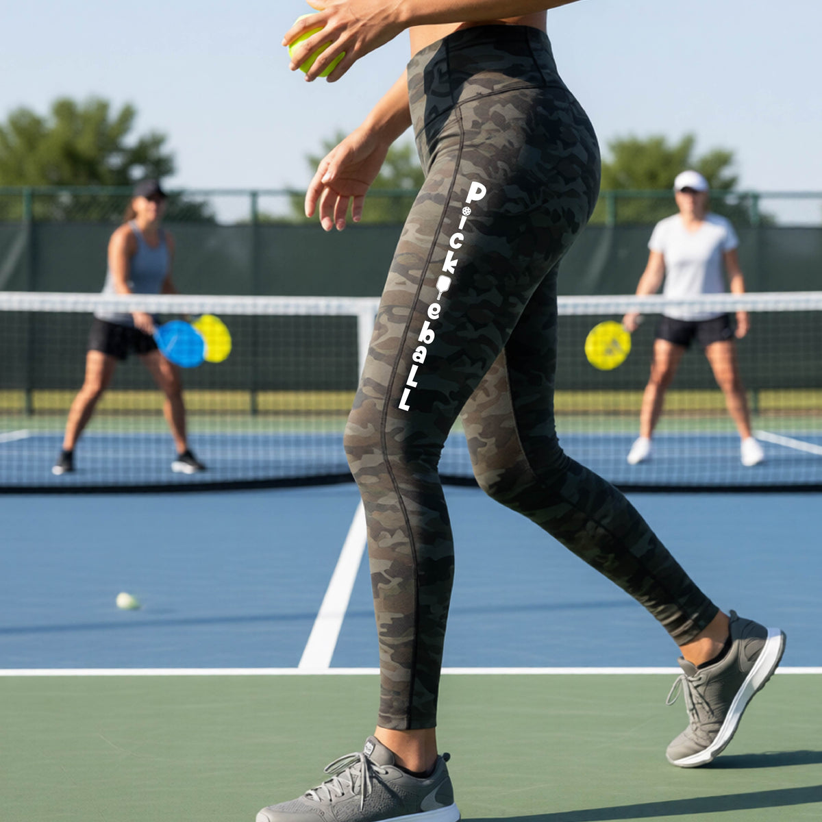 A close-up lifestyle shot of a woman on a pickleball court wearing high-waisted maroon leggings with 'Pickleball' printed in white down the side of her leg.