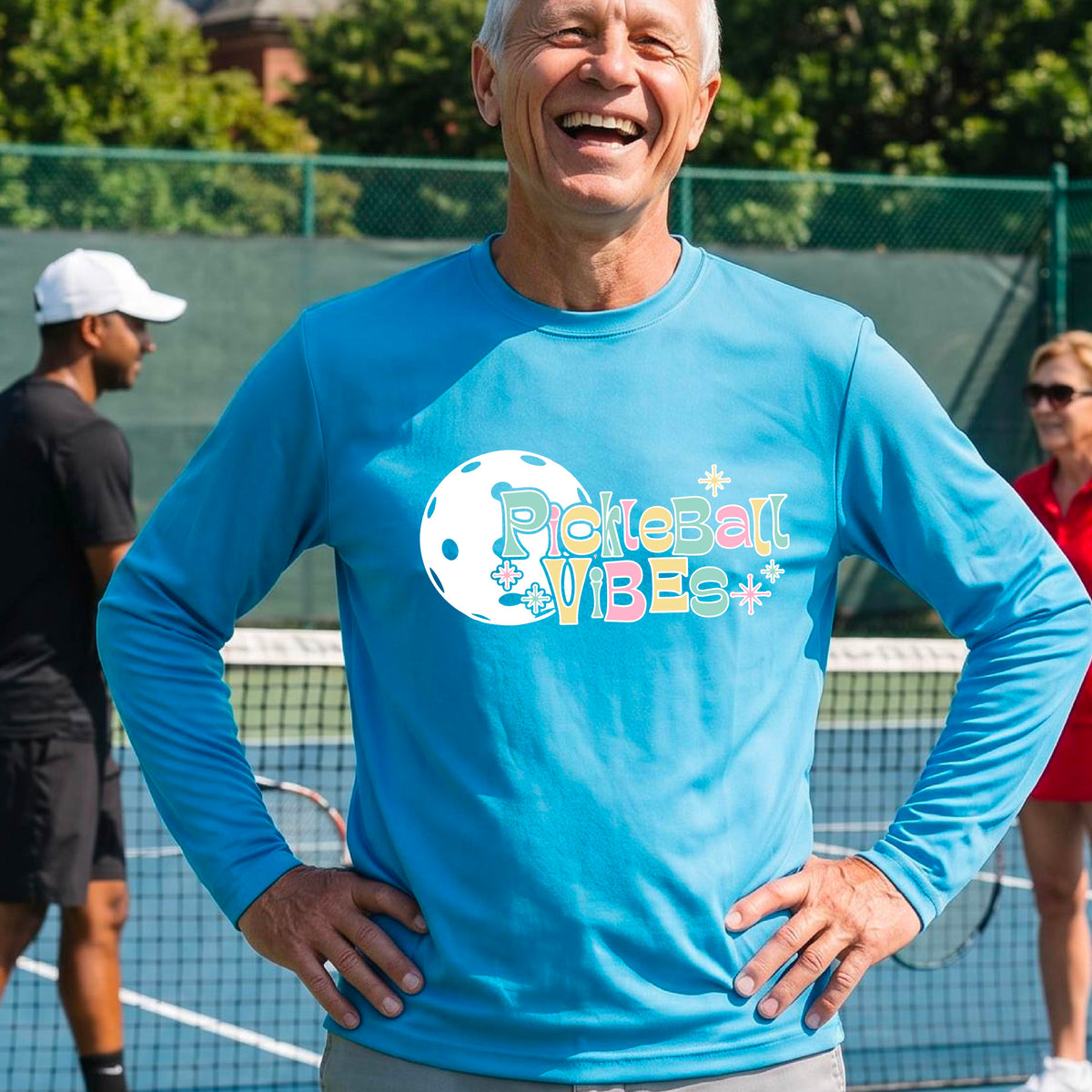 A close-up of a man on a pickleball wearing a bright blue short-sleeve t-shirt, with a colorful retro style font 'Pickleball Vibes' on top of a white pickleball graphic, on the front of the shirt.