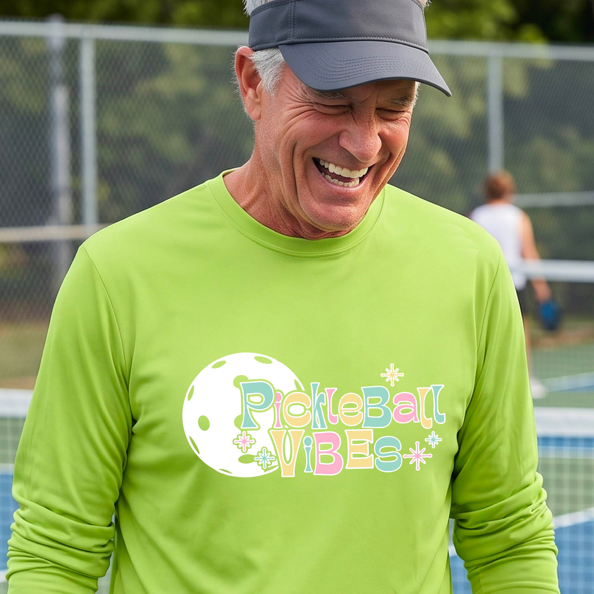 A close-up of a man on a pickleball wearing a lime green short-sleeve t-shirt, with a colorful retro style font 'Pickleball Vibes' on top of a white pickleball graphic, on the front of the shirt.