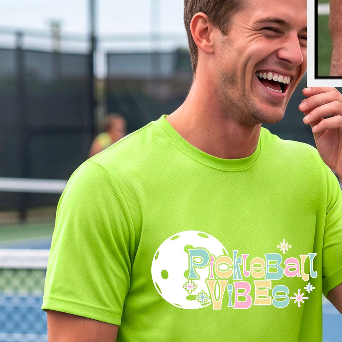 A close-up of a smiling man on a pickleball wearing a lime green short-sleeve t-shirt, with a colorful retro style font 'Pickleball Vibes' on top of a white pickleball graphic, on the front of the shirt.