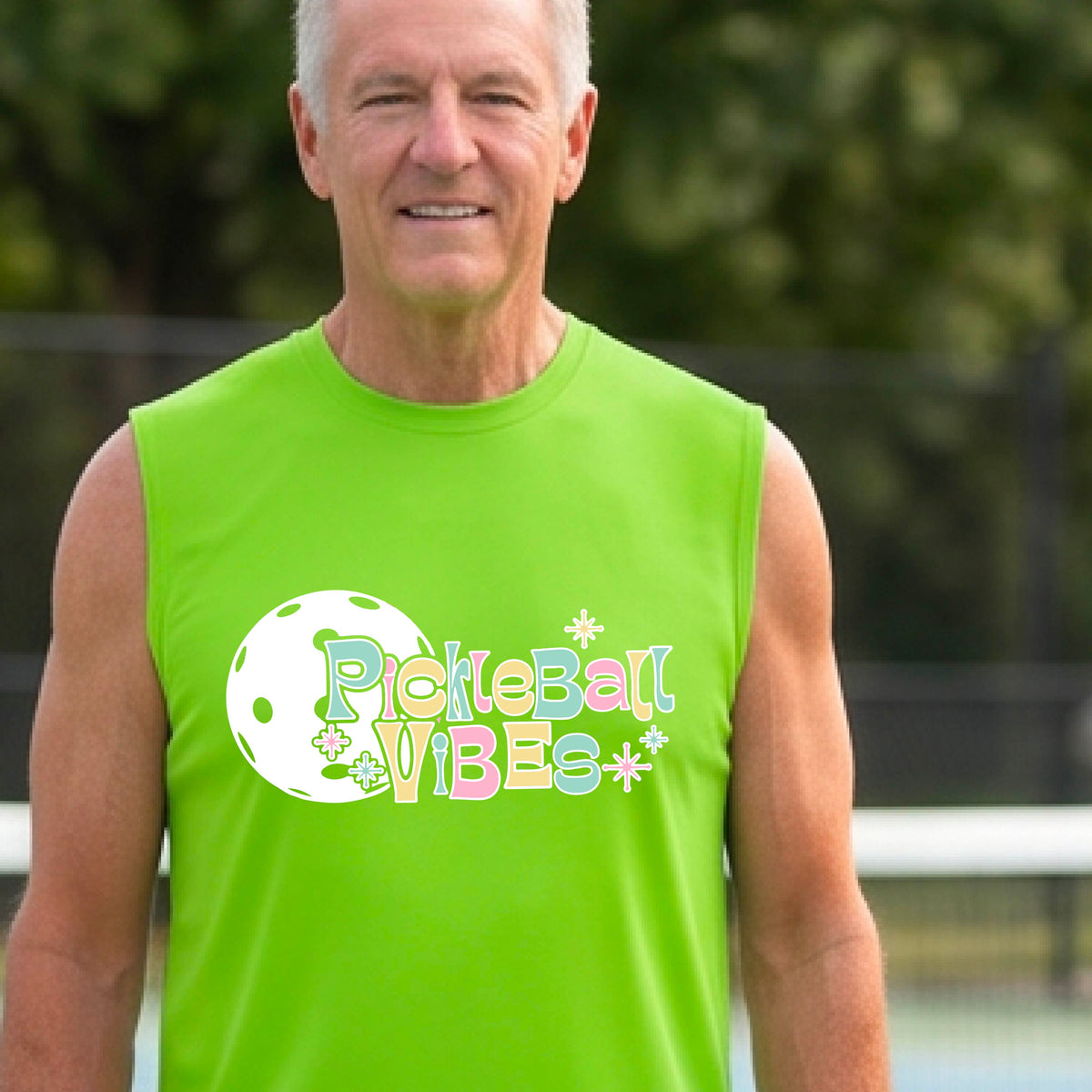 A close-up of a man on a pickleball wearing a lime green sleeveless t-shirt, with a colorful retro style font 'Pickleball Vibes' on top of a white pickleball graphic, on the front of the shirt.
