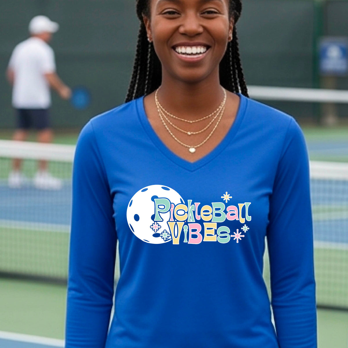 A close-up of a woman on a pickleball wearing a royal blue long-sleeve t-shirt, with a colorful retro style font 'Pickleball Vibes' on top of a white pickleball graphic, on the front of the shirt.