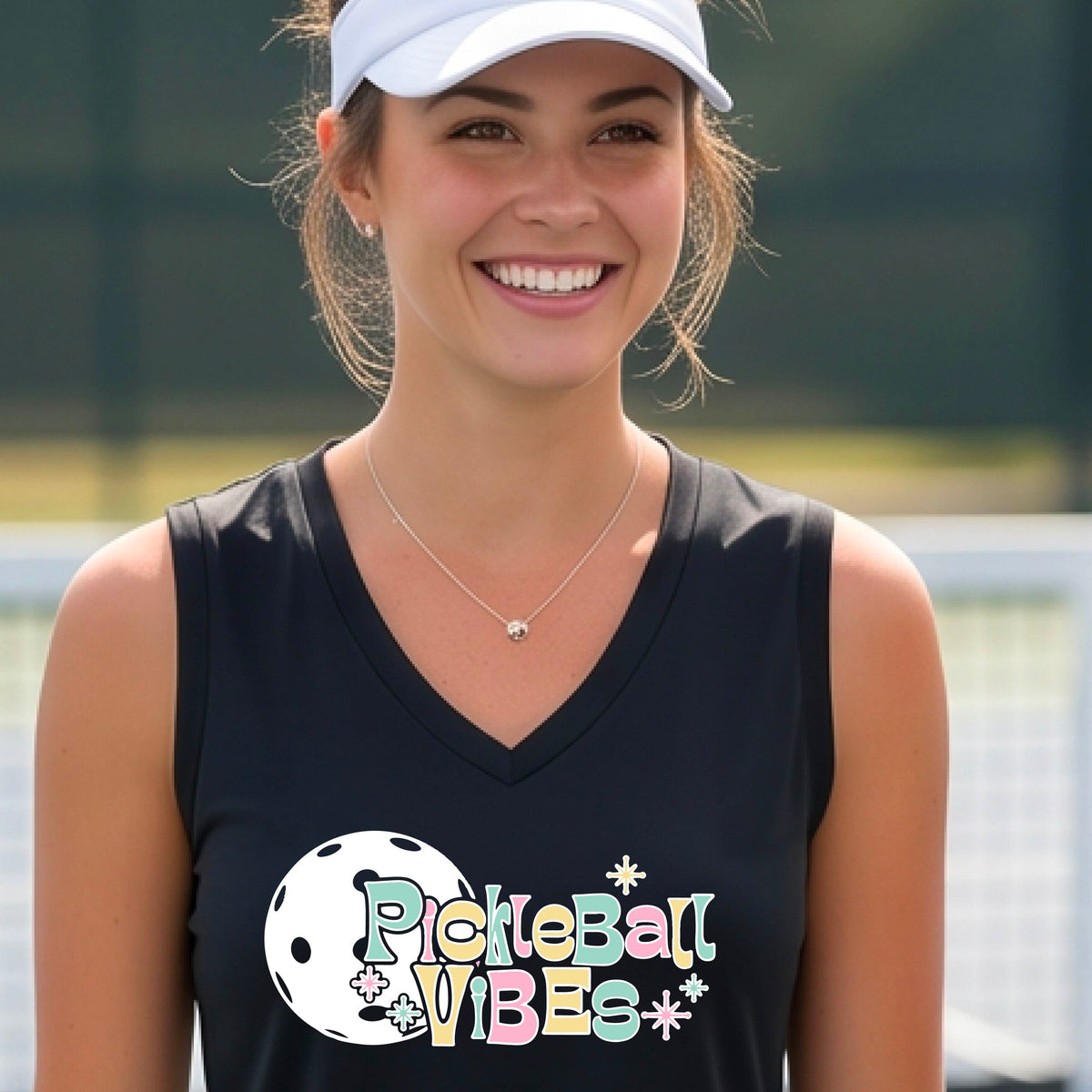 A close-up of a woman on a pickleball wearing a black sleeveless t-shirt, with a colorful retro style font 'Pickleball Vibes' on top of a white pickleball graphic, on the front of the shirt.