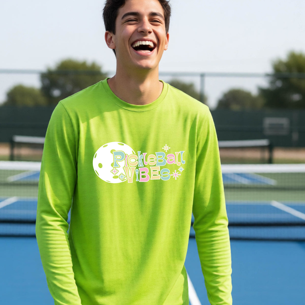 A close-up of a young person on a pickleball wearing a lime green short-sleeve t-shirt, with a colorful retro style font 'Pickleball Vibes' on top of a white pickleball graphic, on the front of the shirt.
