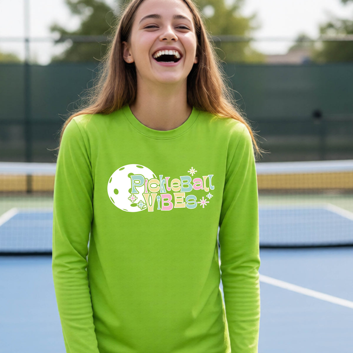 A close-up of a young person on a pickleball wearing a lime green short-sleeve t-shirt, with a colorful retro style font 'Pickleball Vibes' on top of a white pickleball graphic, on the front of the shirt.