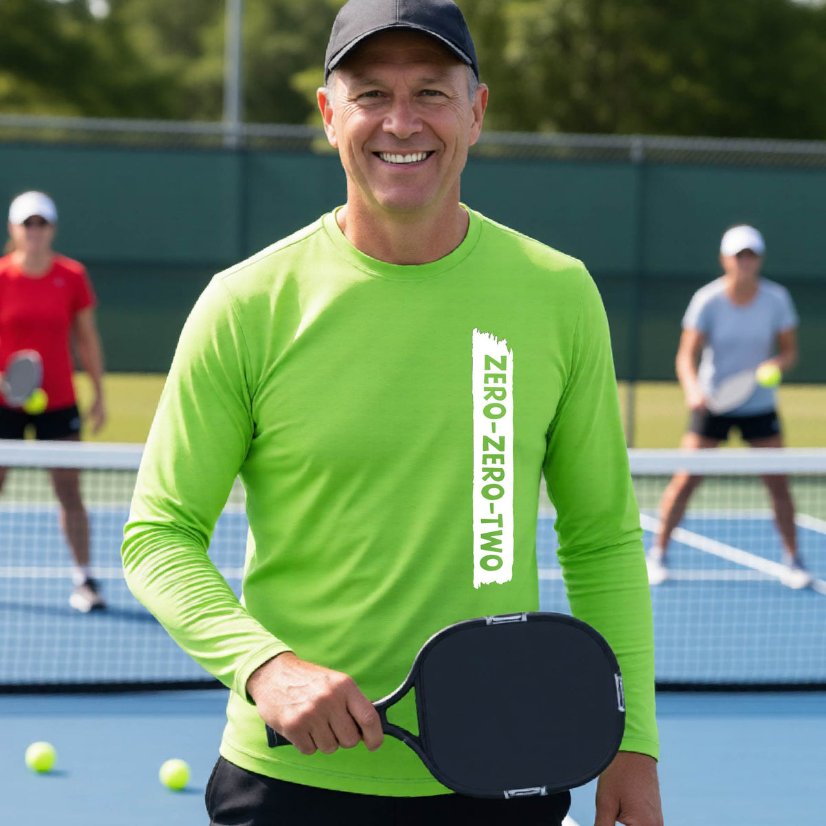 A close-up of a man on a pickleball wearing a lime green long-sleeve t-shirt, with a white graphic of artistic banner with the cutout words of ‘ZERO ZERO TWO’, on the front of the shirt. 