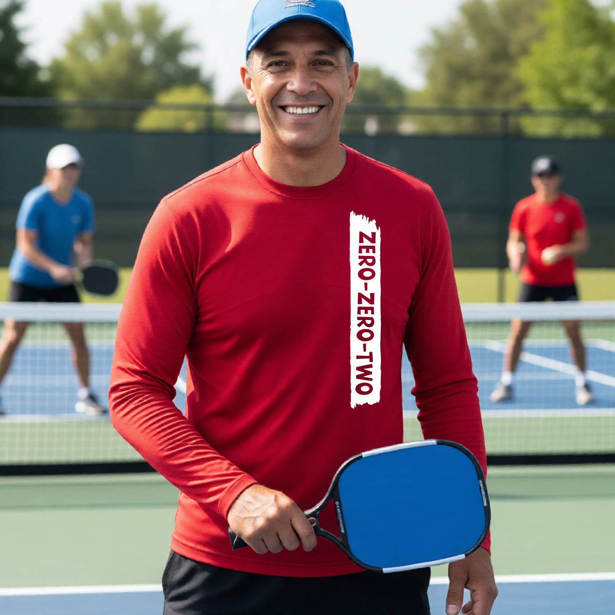 A close-up of a man on a pickleball wearing a red long-sleeve t-shirt, with a white graphic of artistic banner with the cutout words of ‘ZERO ZERO TWO’, on the front of the shirt. 