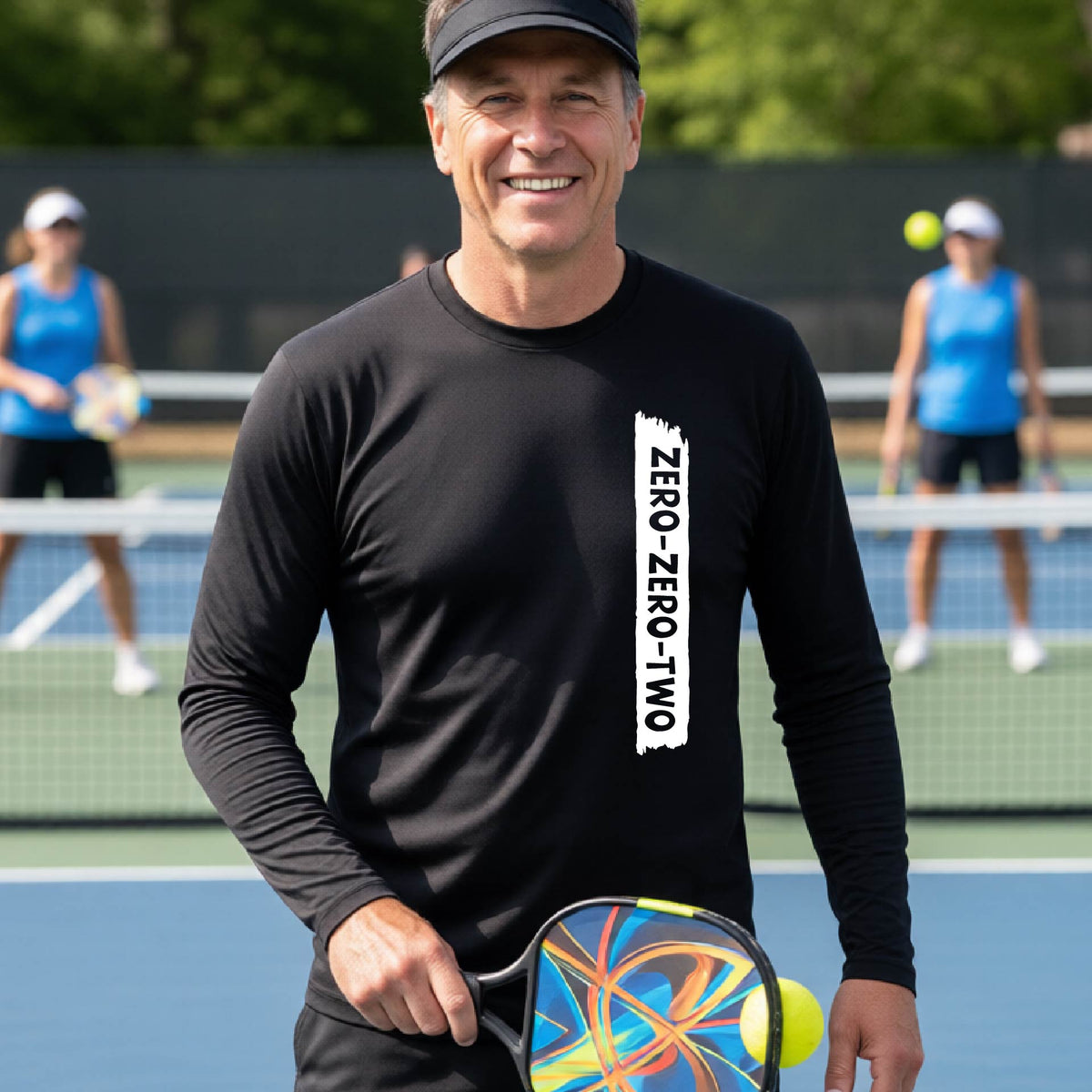 A close-up of a man on a pickleball wearing a black long-sleeve t-shirt, with a white graphic of artistic banner with the cutout words of ‘ZERO ZERO TWO’, on the front of the shirt. 