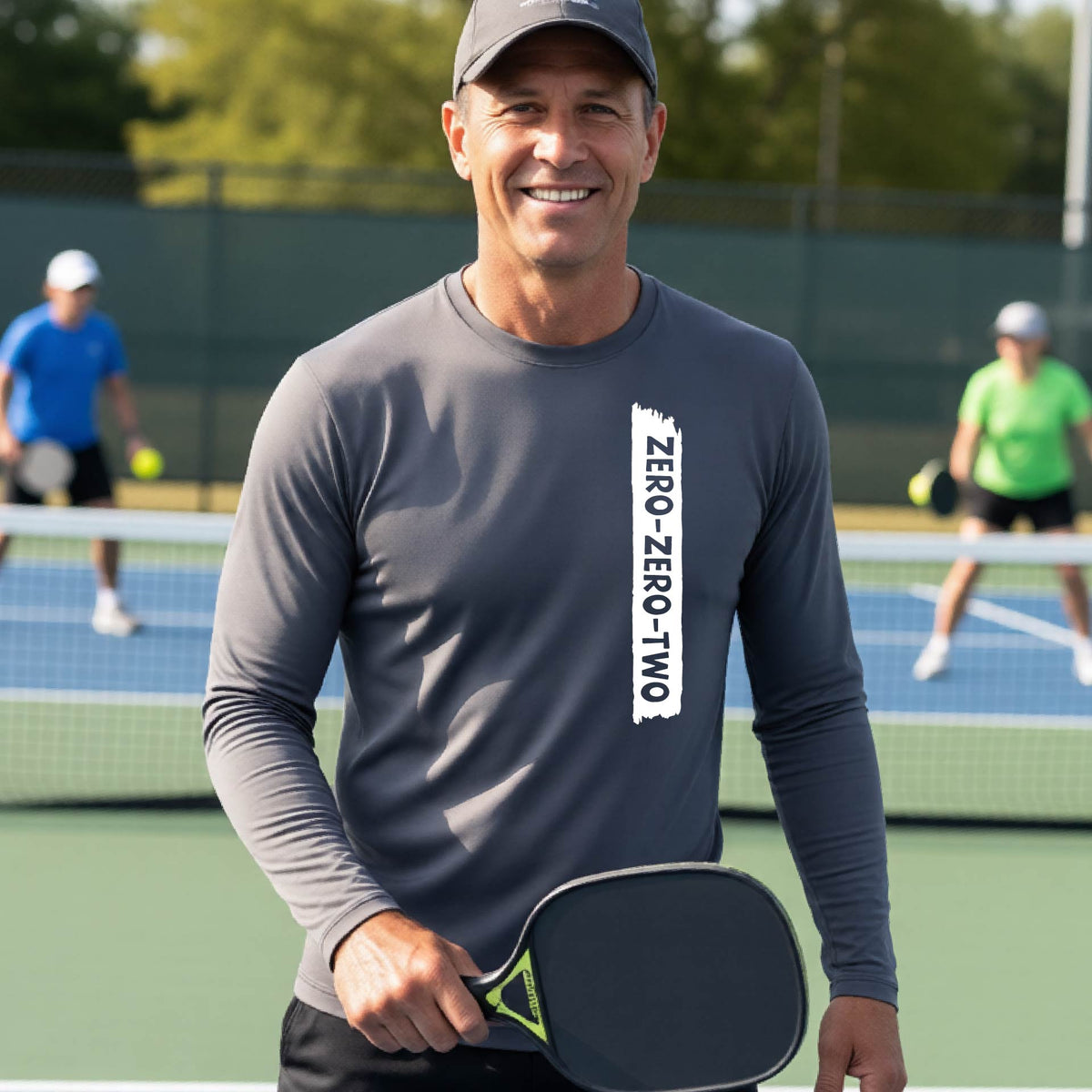A close-up of a man on a pickleball wearing agray long-sleeve t-shirt, with a white graphic of artistic banner with the cutout words of ‘ZERO ZERO TWO’, on the front of the shirt. 