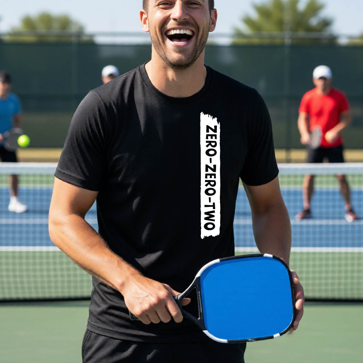 A close-up of a man on a pickleball wearing a black short-sleeve t-shirt, with a white graphic of artistic banner with the cutout words of ‘ZERO ZERO TWO’, on the front of the shirt. 