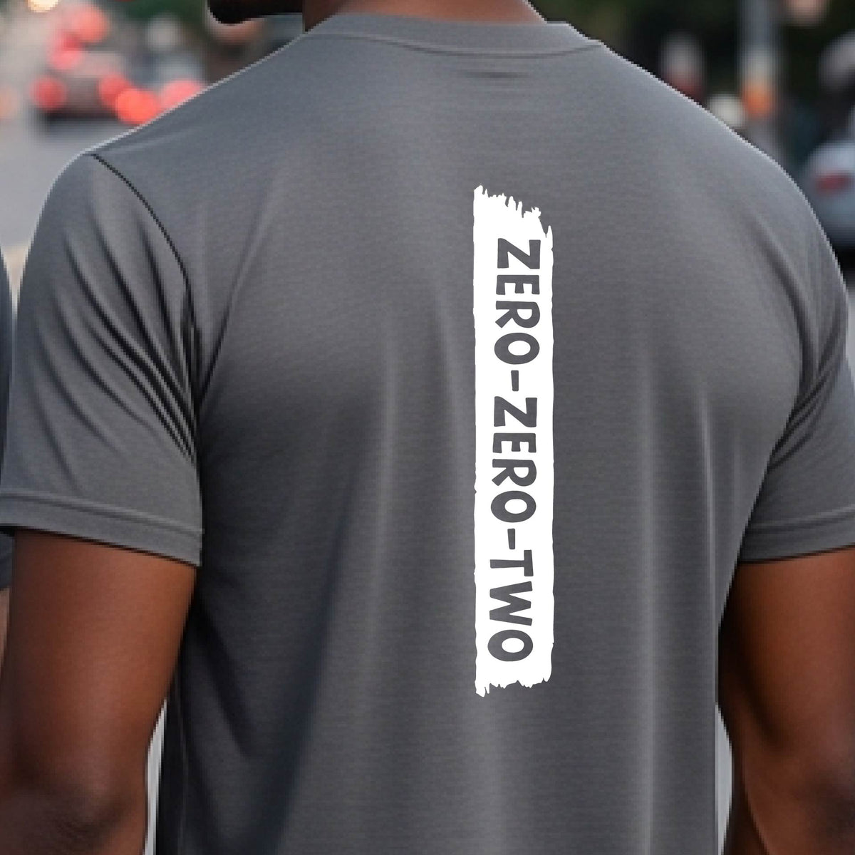 A close-up of a man on a pickleball wearing a dark gray short-sleeve t-shirt, with a white graphic of artistic banner with the cutout words of ‘ZERO ZERO TWO’, on the back of the shirt. 