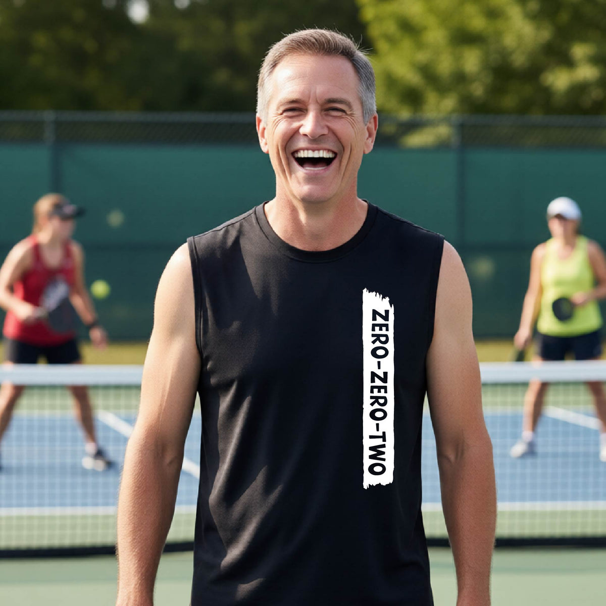 A close-up of a man on a pickleball wearing a black sleeveless t-shirt with a white graphic of artistic banner with the cutout words of ‘ZERO ZERO TWO’, on the front of the shirt. 