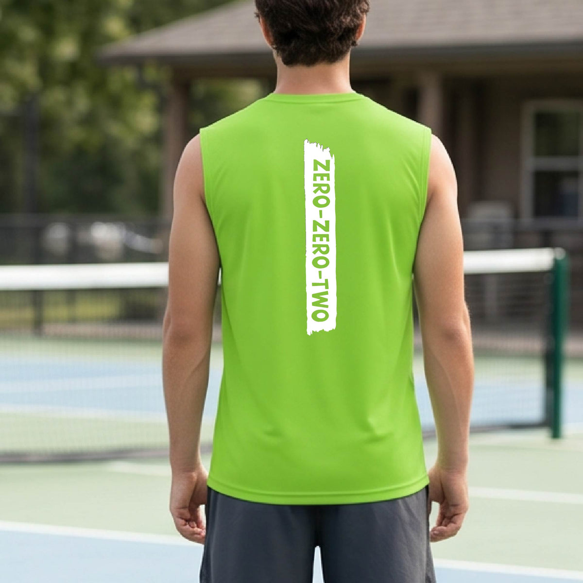 A close-up of a man on a pickleball wearing a lime green sleeveless t-shirt with a white graphic of artistic banner with the cutout words of ‘ZERO ZERO TWO’, on the back of the shirt. 