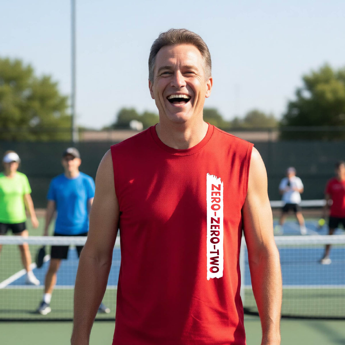 A close-up of a man on a pickleball wearing a red sleeveless t-shirt with a white graphic of artistic banner with the cutout words of ‘ZERO ZERO TWO’, on the front of the shirt. 