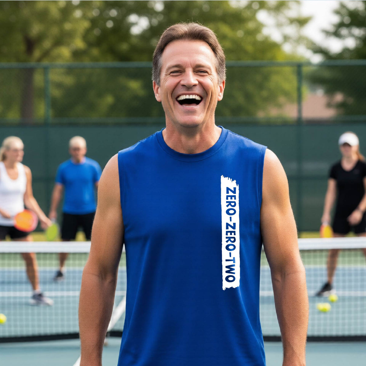 A close-up of a man on a pickleball wearing a royal bluesleeveless t-shirt with a white graphic of artistic banner with the cutout words of ‘ZERO ZERO TWO’, on the front of the shirt. 
