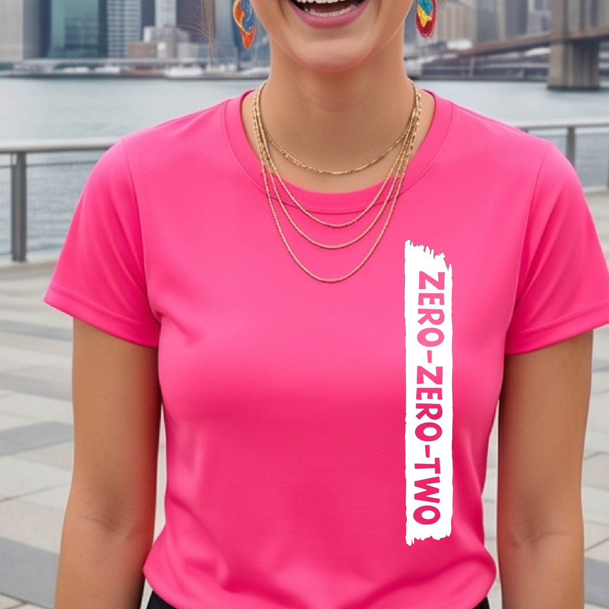A close-up of a woman on a pickleball wearing a pink short-sleeve t-shirt, with a white graphic of artistic banner with the cutout words of ‘ZERO ZERO TWO’, on the front of the shirt. 