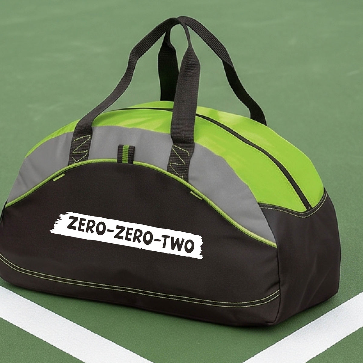 A close-up of a lime green and black duffel bag with gray panels and a white graphic of artistic banner with the cutout words of ‘ZERO ZERO TWO’, on the front. 