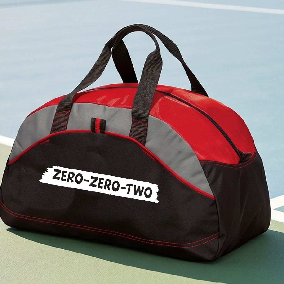 A close-up of a red and black duffel bag with gray panels and a white graphic of artistic banner with the cutout words of ‘ZERO ZERO TWO’, on the front. 